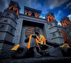 a statue of a man sitting in front of a castle with an orange sash around his neck