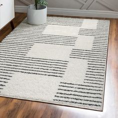 a white rug with black lines on it and a potted plant in the corner