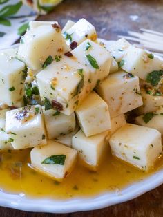 a white plate topped with cubed potatoes covered in olive oil and garnished with herbs