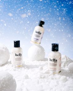 three bottles of body lotion sitting in the snow next to a snowball and blue sky