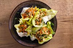 a bowl filled with lettuce and carrots on top of a wooden table