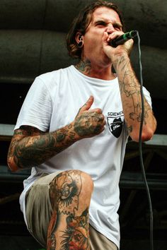 a man with tattoos on his arms and legs, holding a microphone up to his mouth