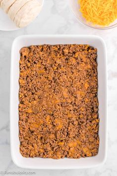 a casserole dish filled with ground beef and cheese next to two tortilla shells