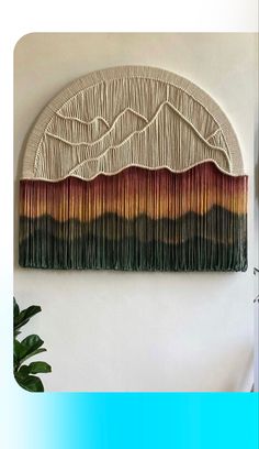 a wall hanging made out of yarn and fringes with a plant in the foreground