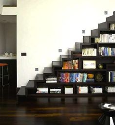 a living room filled with furniture and a book shelf next to a stair case full of books