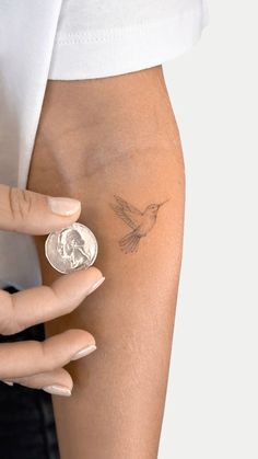 a woman's hand with a small tattoo on her left arm and a coin in the other hand