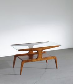 a table with a glass top and wooden frame on the bottom, in front of a white wall