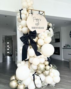 a birthday decoration with balloons and black bows on it's pole in a living room