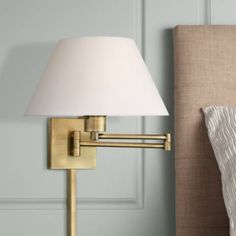 a lamp on a wall next to a bed with a beige headboard and pillow