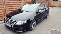 a black car is parked in front of a wooden fence and brick driveway area,