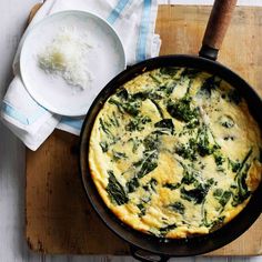 an omelet with spinach and cheese in a skillet on a cutting board