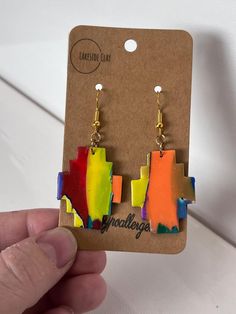 a pair of colorful earrings is being held by a person's hand in front of a card