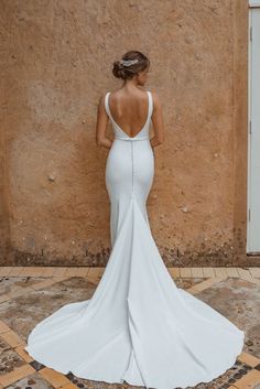 a woman standing in front of a wall wearing a white dress with backless straps