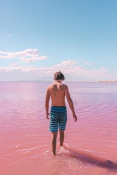 a man standing in the water with his back to the camera, looking at the pink lake