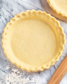 two pie crusts sitting next to each other on a marble counter top with wooden utensils