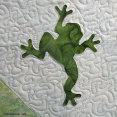 a green frog sitting on top of a quilt