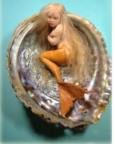 a little mermaid doll sitting on top of a seashell in the shape of a shell