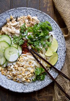 a bowl filled with noodles, cucumber slices and other vegetables next to chopsticks