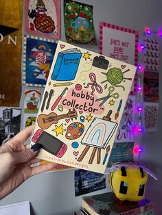 a person holding up a book in front of a wall with many pictures on it