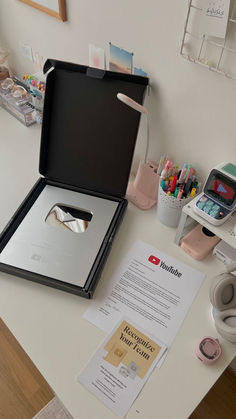 an open black box sitting on top of a white table next to some pens and pencils