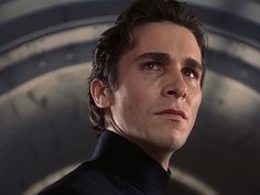 a man in a black suit looks off into the distance with his eyes wide open