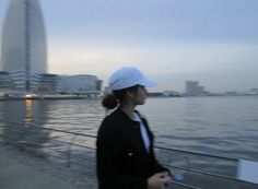 a woman is walking along the water in front of some buildings and skyscrapers at dusk