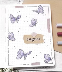 an open notebook with butterflies on it next to some markers and pencils that read august