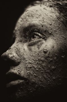 a woman's face covered in mud with her eyes open and one eye partially closed