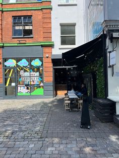 an empty sidewalk with tables and chairs in front of a building