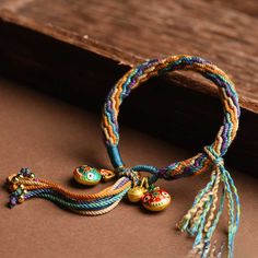 two bracelets with bells and tassels on top of a wooden table next to a piece of wood