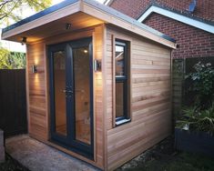 a small wooden shed with its door open and windows closed on the outside, in front of a brick house