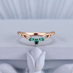 a ring with two green stones on it sitting on top of a white cloth covered box