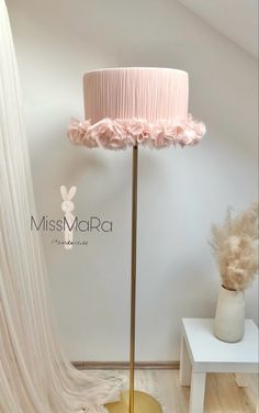 a floor lamp with a pink shade on top and flowers in the bottom, next to a white table