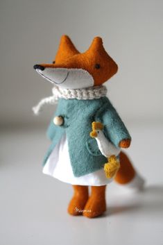 a small stuffed animal wearing a coat and hat with a flower in its hand, on a white surface