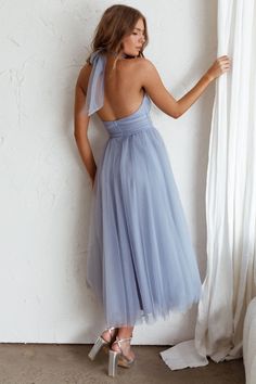 a woman in a blue dress leaning against a white wall with her back to the camera