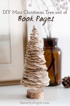 A little Christmas tree decoration made out of old book pages, sitting on a shelf with a vase of branches in the background