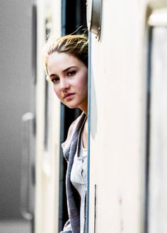 a young woman leaning on the side of a train door looking out at the camera