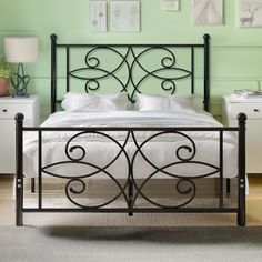 a black metal bed frame with white sheets and pillows in a green walled bedroom area