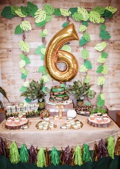 a table topped with cake and cupcakes next to a number 6 balloon on top of a wooden wall