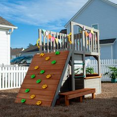 a wooden play set with a climbing wall and potted plants on the bottom level