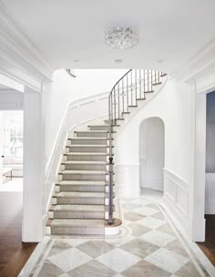 a staircase in a house with white walls and wood flooring is flanked by a chandelier that hangs from the ceiling