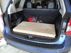 the back end of a blue car with a wooden board in it's trunk