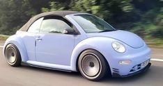 a blue car driving down the road with trees in the background