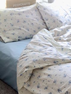 an unmade bed with blue and white flowers on the comforter next to a stack of books