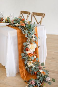 an orange table runner with flowers and greenery on the top is ready to be served