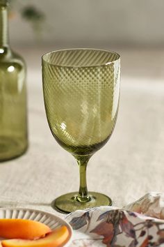 a green wine glass sitting on top of a table next to a plate with an orange slice