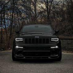 the front end of a black jeep parked in a parking lot with trees behind it