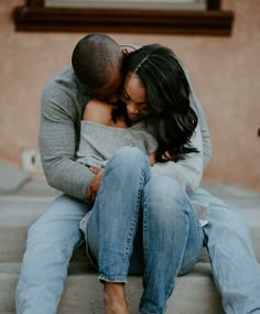 a man and woman sitting on the ground hugging each other with their arms around each other