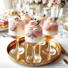 there are four desserts in glasses on the table with gold rimmed plates and silverware