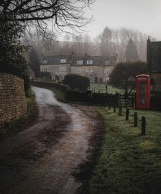 a dirt road in front of houses on a foggy day with a red phone booth